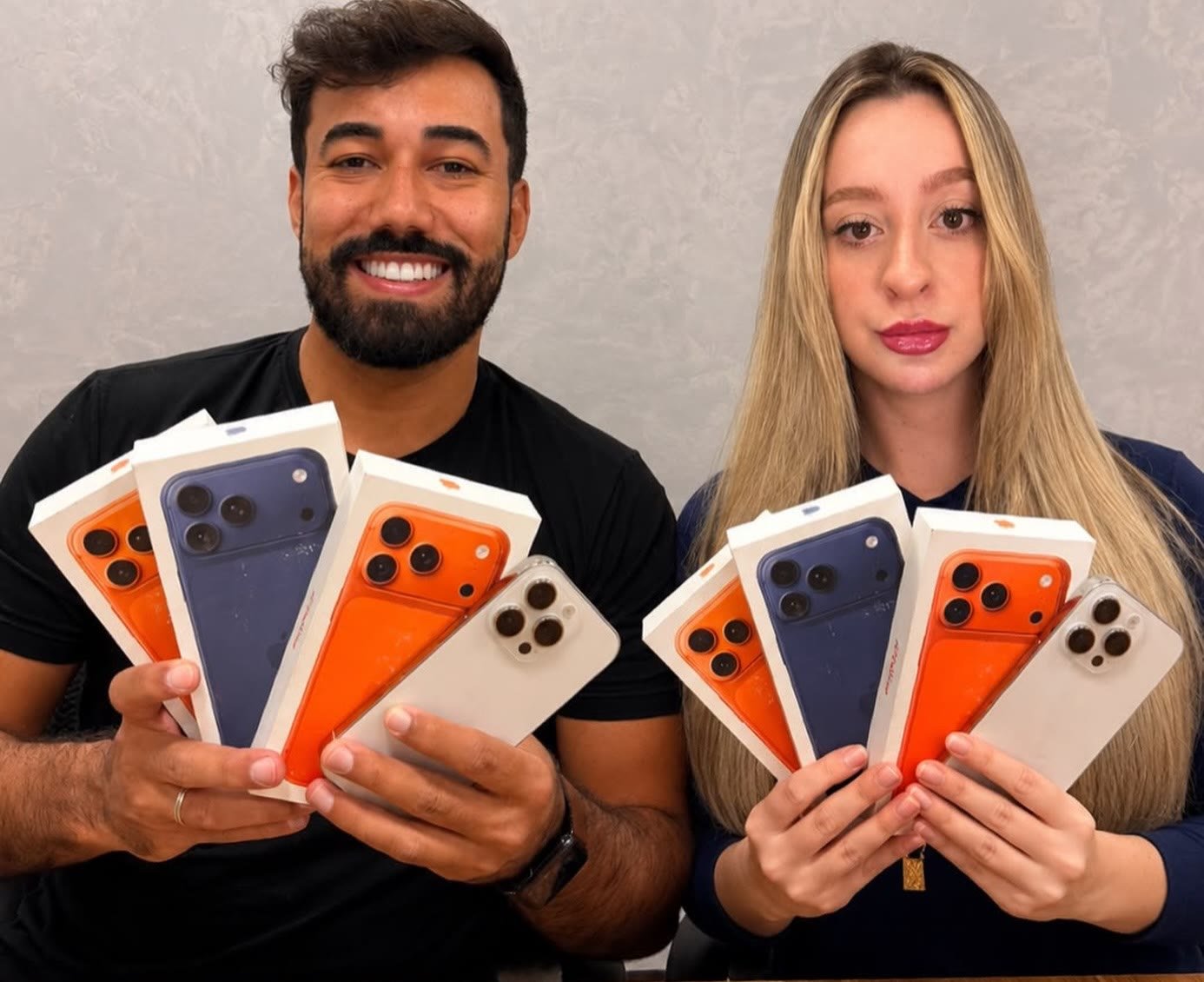 Equipe da loja segurando caixas lacradas do iPhone 17 Pro nas cores laranja, azul e prateado